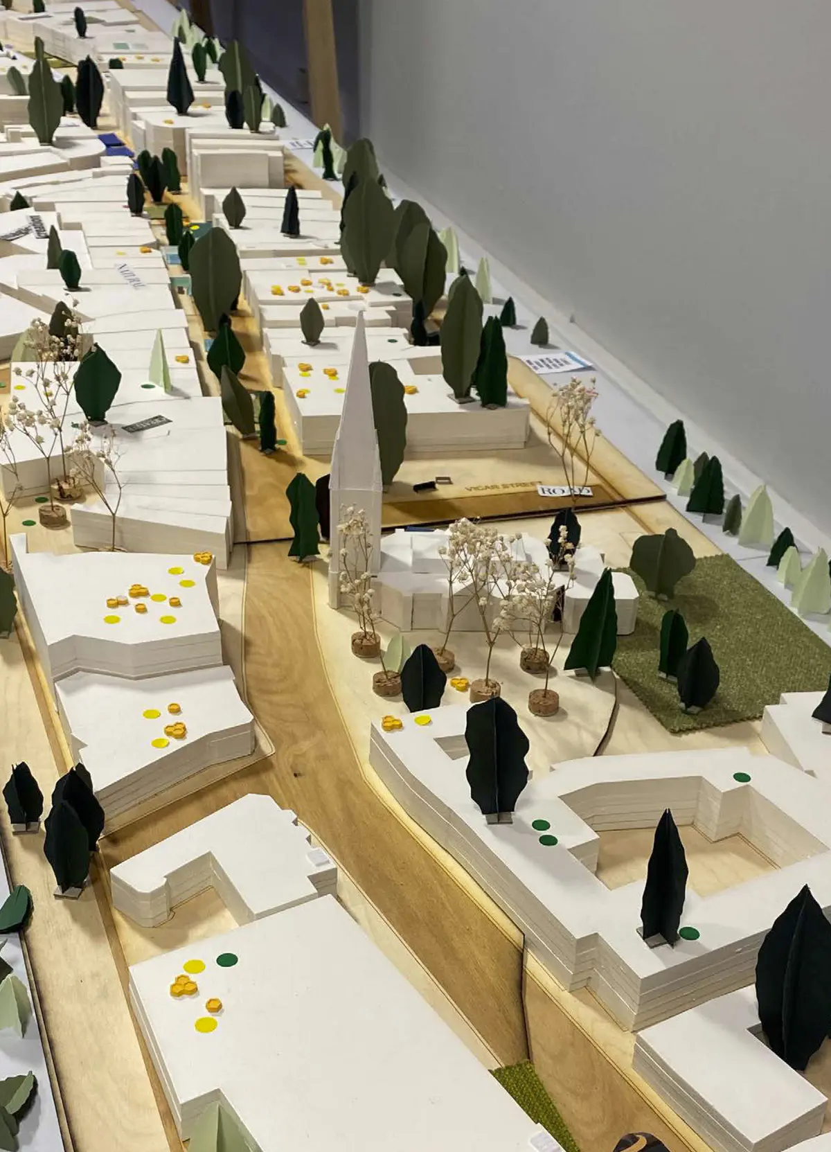 Looking to be the centrepiece of our exhibition, we proposed to create a site model of Dudley Highstreet at 1:200 scale with buildings modelled in a simple form. Local residents and visitors to the exhibition are then invited to decorate a chosen building to how they would envision it sat within the context of a greener Highstreet. We want to tie in our themes of biodiversity and materials by proposing that buildings can, and do, have the potential to be a lot healthier, sustainable, and interactive on the street. This site model also helps gain vital public opinions on the Highstreet and prompts discussion of areas most in need of attention.

To ensure that the model is utilising the MDF to the most efficient standard possible. First, the centres of the massing blocks have been hollowed out. This allows a reduction in materials used as other buildings can be cut in the centres of the model. Then the top is finished with a solid piece.
The waste material is placed into the recycling rack where other students can reuse it; otherwise, if the material left cannot be used for another project, it is recycled correctly by the university.

The model spanned just over 3.4m long and over 50cm wide. With the majority being cut from scrap woods that would fit the jigsaw of the shape, we were able to drastically cut down on waste. We also got some small benches and bee hives printed from recycled plastics, and used dried flowers as trees to represent the green spaces. Ultimately, the model seemed like a huge success, and really helped portray our ideas about Dudley High Street to those who came by. Everyone from Dudley who saw the model knew that it was the High Street, and interacted well with it. The size did make it difficult to move, especially to carry to the site, but it sat nicely in the centre of the the room and really drew people in to interact with it.

The model brought people in from outside to play with, write on, interact with. It became a spectacle for the public to come in and see what was happening and offer their ideas about what could be done.

The event was a success. Many people from the public (those who heard about the event, and those who just happened across it on the day) came in to interact with the model, which sat as the centre piece in the room. Kids liked to play with the pieces while the adults talked about things that could come from actions to help the High Street, not just leave it as is.

SOME OF THE KEY IDEAS WERE:
- The Shops need to be inviting for everyone. It’s no good having these places to go if people would rather take a bus to the next town.
- Just putting up boards across the windows is awful. Paint, Posters, Graffiti: Anything that actually makes the High Street look still alive is better than just wooden boards.
- More Green is needed. While it is obvious that there is a lack of Trees, many people wanted to push for these small bushes or planting spaces that could easily be implemented across the street.
- Spaces for public events or for people to at least gather at. While there is the Market and Fountain, it is not enough for the people of Dudley.
- Something needs to be done about the cars on the High Street. Some were Pro-Removal of all Cars, while some just wanted to limit when they could access the High Street.

Following the exhibition we created a series of drawings with our own interpretation of Sarah Wigglesworth ‘The Dining Table’ drawing. The drawings are a perfect representation of the our interactive model at the ERA Environmental Exhibition and Event. Showing the interaction the public had with the model, as well as the conversations that were held around the model. - Table 1.png